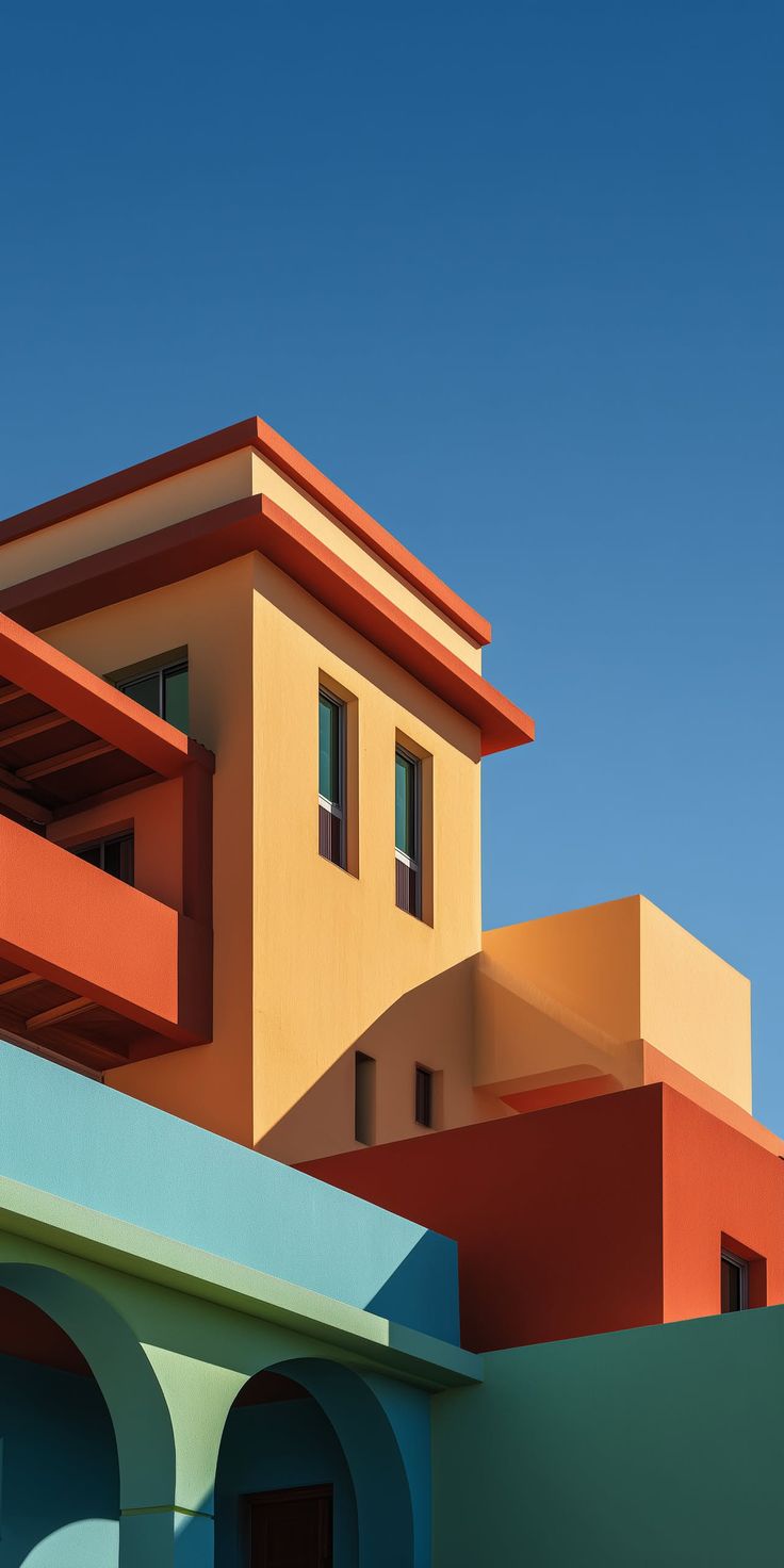 Photograph depicting A vibrant architectural composition featuring geometric buildings in bold primary and secondary colors set against a clear blue sky.